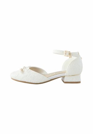 Chaussure blanche en dentelle à petit talon avec bride à la cheville, boucle dorée et petit nœud décoratif sur l’orteil, vue de profil sur fond blanc.