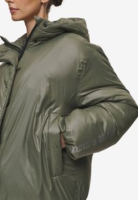Pufferjack in donkergroen olijfgroen, met een capuchon, ritssluiting aan de voorkant en oversized mouwen. Geweven glanzende stof met zijzakken.