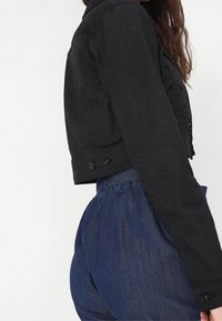 Svart kort denimjacka med knäppning fram, med krage och långa ärmar. Bärs ihop med högmidjade blå denim byxor.