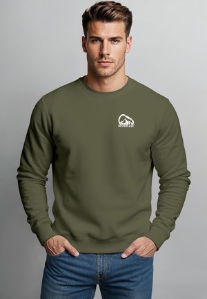 Junger Mann mit kurzen Haaren, der einen olivgrünen Sweatshirt mit Karabiner- und Berglogo und dem Wort "NEVERTHELESS." trägt