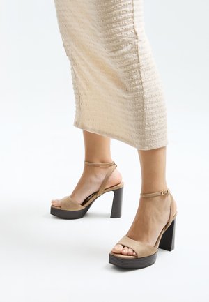 Beige suede heeled sandals with a platform sole, ankle strap, and textured brown block heel. Open-toe design with visible toes.