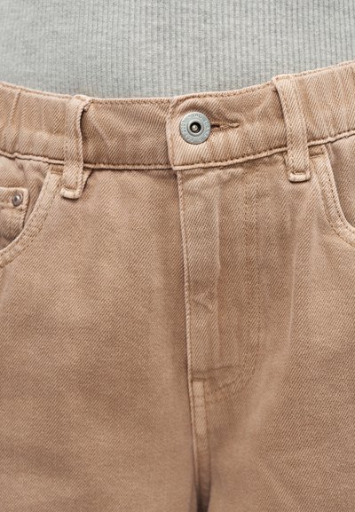 Μπεζ τζιν από τζιν ύφασμα με μέση που κλείνει με μεταλλικό κουμπί, θηλιές για ζώνη και τσέπες, φορεμένο με γκρι ανοιχτού χρώματος κορυφή με ρίγες.