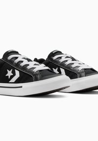 Baskets en toile noires avec des lacets blancs, un logo d'étoile blanc et un contour noir contrastant sur la semelle. Semelle en caoutchouc plate et languette rembourrée.