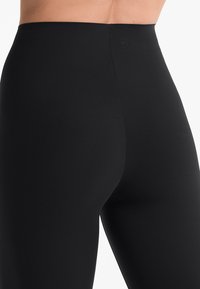 Leggings noirs taille haute fabriqués dans un tissu lisse et extensible avec un design sans coutures. Présente des détails de logo subtils au niveau de la taille.
