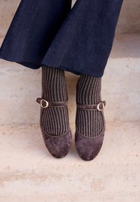 Chaussures Mary Jane en daim marron avec une boucle accent dorée, associées à des chaussettes rayées foncées avec des fils métalliques, portées avec un pantalon à jambes larges.