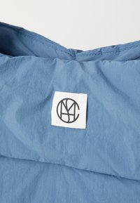 Col haut de veste rembourré en tissu bleu doux avec une texture lisse ; présente une étiquette blanche avec un logo noir, mettant en valeur le design.