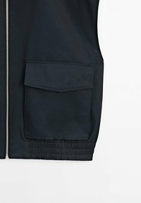 Czarna, lekka kurtka z zamkiem błyskawicznym z przodu, z dużą kieszenią naszywaną i elastyczną talią, co zapewnia dopasowany wygląd. Gładka tekstura.