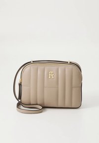 Beige crossbody taske med quiltet detaljer, guldfarvet hardware og sort kant. Har en lynlåslukning øverst og en justerbar rem.