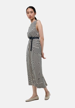 Robe midi rayée en noir et crème, avec des motifs géométriques, une ceinture à la taille et un design sans manches. Texture de tissu douce.