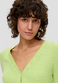 Cardigan côtelé vert clair avec un col en V et une fermeture à boutons sur le devant. Le tissu a une finition légèrement texturée et une silhouette ajustée.