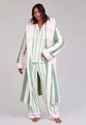Vrouw draagt pastelgroen-wit gestreepte pyjama met roze accenten en een lange, pluizige gestreepte kamerjas in bijpassende kleuren.