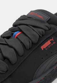 Black Puma Suede XL sneaker with thick black laces and red and blue stripe detail on tongue and side logo.