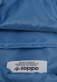 Tessuto blu con una texture liscia, caratterizzato da un'etichetta bianca con testo nero che indica il marchio e le istruzioni per la cura. Bordo cucito visibile.