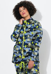 Kamelånga jacka i blå och gröna nyanser med gula stjärnmönster. Har en hög krage och en ljus dragkedja, kombinerad med matchande byxor.