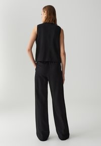 Top senza maniche nero e pantaloni a gamba larga in tessuto leggero, caratterizzati da una vestibilità rilassata e un design minimale, visti da dietro.
