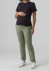 Svart kortärmad topp med spetsdetalj, matchad med ljus olivgröna byxor med elastisk midja och vita sneakers. Avslappnat plagg, figurnära siluett.