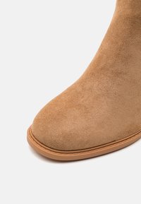 Bottine en daim camel avec un bout arrondi, une texture lisse, et une semelle en caoutchouc avec un léger liseré camel. Aucun élément métallique ni motif visible.