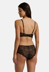 Černá krajková souprava prádla obsahující braletku s nastavitelnými ramínky a odpovídajícími kalhotkami typu boyshort. Květinový vzor a jemné vlnité okraje.