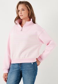 Felpa di colore rosa chiaro con colletto alto, chiusura con zip a metà, e strisce orizzontali di colore verde chiaro. Materiale in cotone, vestibilità comoda, polsini a coste.