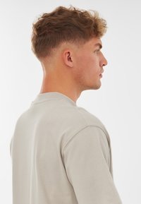 Világosszürke pulóver, kerek nyakkivágással, látható varrással és laza szabással. Az anyag lágy és sima tapintású.