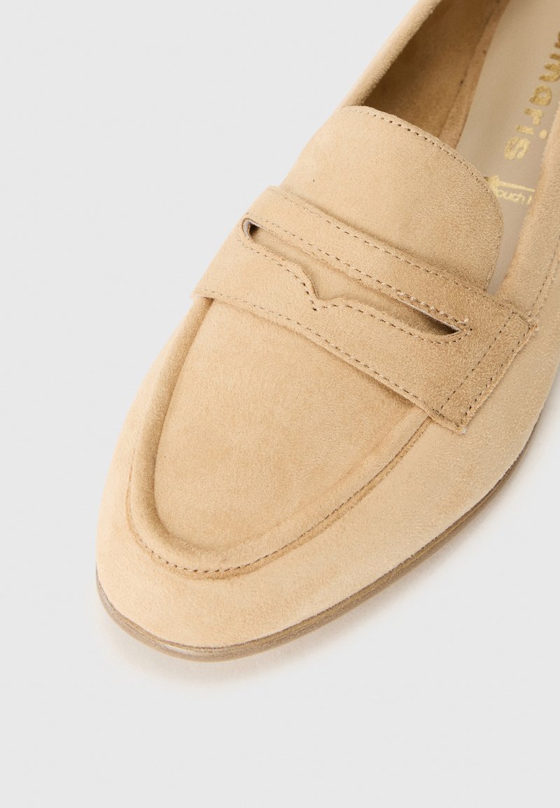 Beige Wildleder-Loafer mit einer abgerundeten Zehenpartie und einem dekorativen Riemenakzent. Besitzt eine Naht entlang der Kanten und eine glatte, strukturierte Oberfläche.