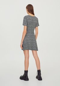 Vestido corto en blanco y negro con un corsé ajustado y falda acampanada. Tejido ligero con un sutil patrón floral. Un par de botas negras de suela gruesa.