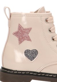 Botín de tobillo beige brillante con apliques de estrella de purpurina rosa y corazón de purpurina negra; presenta punta redonda y detalles de costura contrastantes en la suela.