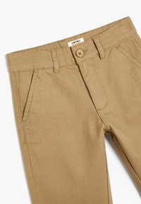Chinos de algodón caqui con una textura suave, cinturilla estándar, cierre de botones, bolsillos laterales y un único pliegue frontal.