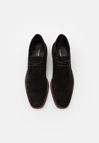 Scarpe in suede nere con un design elegante, punta arrotondata e suola marrone a contrasto. Presentano lacci grigi e un interno in pelle liscia.