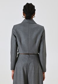 Blazer gris cropped en tissu texturé avec des manches longues et un col à revers. Présente une taille cintrée et un éclat subtil.