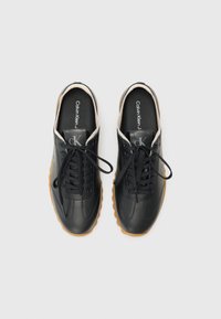 Sneakers in pelle nera con superficie testurizzata, dotate di lacci rotondi e suole in gomma. All'interno, la soletta mostra il marchio "Calvin Klein".