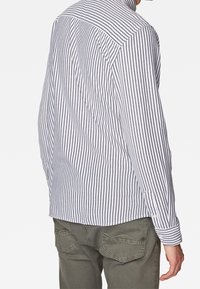 Camisa de manga larga a rayas en blanco y azul marino, con un corte entallado, puños con botón y dobladillo curvado. Lleva encima un pantalón de color verde oliva.