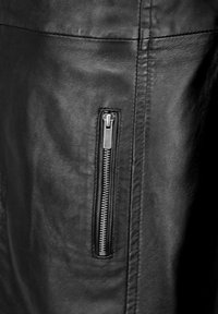 Schwarze Lederjacke mit einer vertikalen Reißverschlusstasche an der Seite, glatter Textur und schlankem Design mit dezenten Nähdetails.