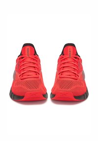 Scarpe da ginnastica rosse con una tomaia in rete traspirante, progettate per il comfort. Accenti neri sulla suola e sul tallone; i lacci sono piatti e ben visibili.