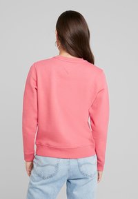 Rosa sweatshirt med rund hals och ribbade ärmuppslag, med en mjuk yta och en något avslappnad passform, tillsammans med ljusblå jeans.