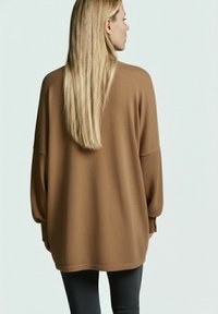 Brauner übergroßer Pullover mit langen Ärmeln, strukturiertem Stoff und gerundetem Saum, kombiniert mit schwarzen, engen Hosen.