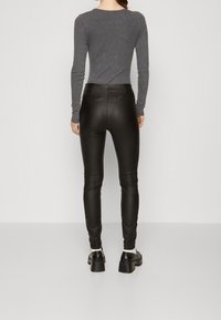 Svarta fusk läder skinny byxor med hög midja, med en slät yta och bakfickor. Matchas med en tät grå långärmad topp.