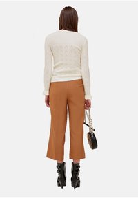 Kremowy sweter z dzianiny z prążkowanymi mankietami, brązowe krótke spodnie i czarne botki na obcasie. Nosi okrąłą czarną torebkę na łańcuszku.