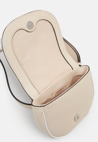 Béžová malá křížová taška Calvin Klein s otevřeným klopou, magnetickým uzávěrem a podšívkovou vnitřní kapsou.