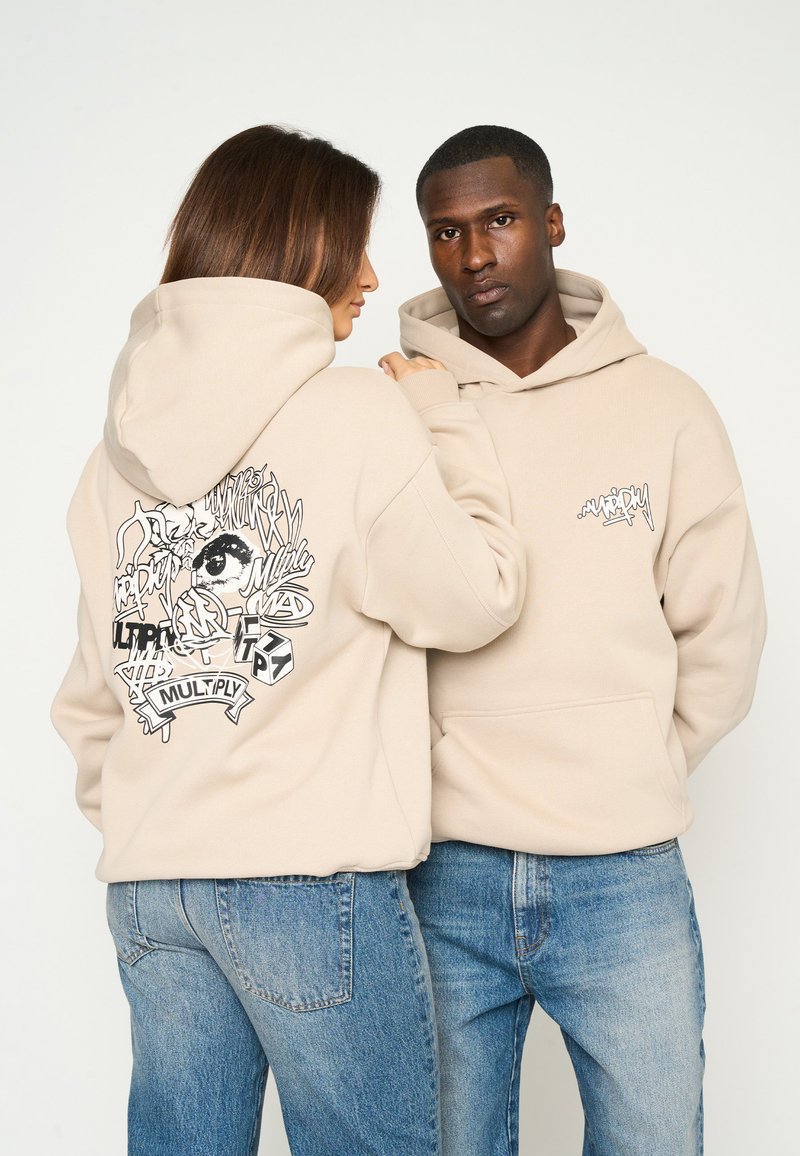 Sweatshirts beige avec un design graphique au dos en encre noire et un petit logo à l'avant. Coupe décontractée avec poches kangourou.