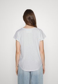 Světle šedé tričko s krátkým rukávem, kulatým výstřihem a zakřiveným lemem. Měkká, strukturovaná tkanina s uvolněným střihem a bez viditelného loga.