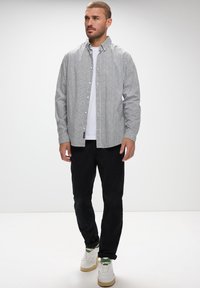 Camisa de botones gris con patrón y cuello doblado, camiseta blanca debajo, combinada con pantalones negros y zapatillas blancas.