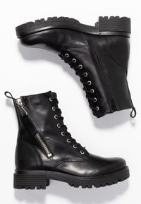 Bottes en cuir noir montant à la cheville, avec un bout arrondi, une fermeture éclair latérale, un laçage devant, une semelle texturée et des détails en métal argenté contrastant.