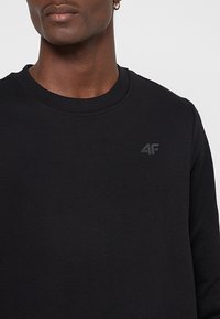 Czarna bluza z okrągłym dekoltem, wykonana z teksturowanego materiału, z subtelnym czarnym logo 4F na lewej stronie klatki piersiowej.