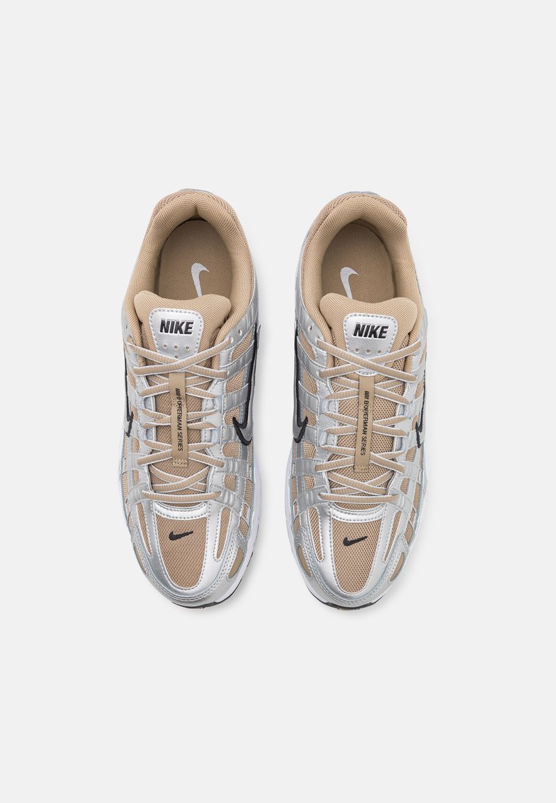 Trampki Nike z siateczkowym wierzchem w kolorze srebrnym i beżowym, czarnymi akcentami oraz teksturowaną podeszwą. Posiadają wyraźne logo na języku.