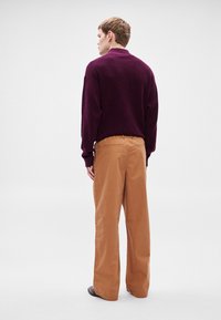 Bordó kötött pulóver bézs, bő szárú nadrággal, amely elasztikus derékpánttal rendelkezik. Simább textúra és kényelmes, laza fazon.