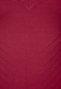 Viininpunainen neulottu kangas siksakkuviivakuviolla, jossa on sileä pinta ja V-muotoinen yksityiskohta pääntiellä.