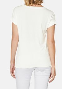 Camiseta blanca de manga corta con cuello redondo y puños enrollados. Tejido suave, ajuste ligeramente holgado y dobladillo curvado en la parte posterior.