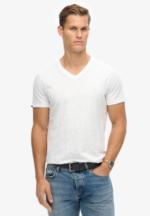 Witte katoenen v-hals t-shirt met korte mouwen, gecombineerd met blauwe spijkerbroek en een zwarte riem. Het ontwerp is eenvoudig met een losse pasvorm.