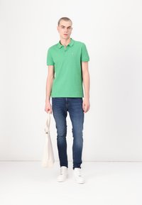 Grønn bomull polo skjorte med krage, sammen med slim-fit blå jeans og hvite sneakers, holder en kremfarget tote bag.
